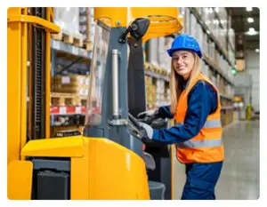 A young woman with blonde hair operating a forklift in a warehouse, wearing safety gear.