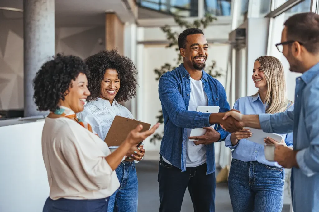 Several people are greeting each other while holding clipboards in business casual clothing.